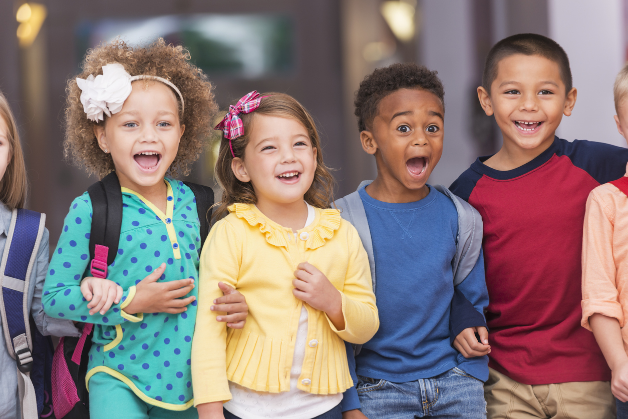 Group of young children smile at their parents after first day of school.