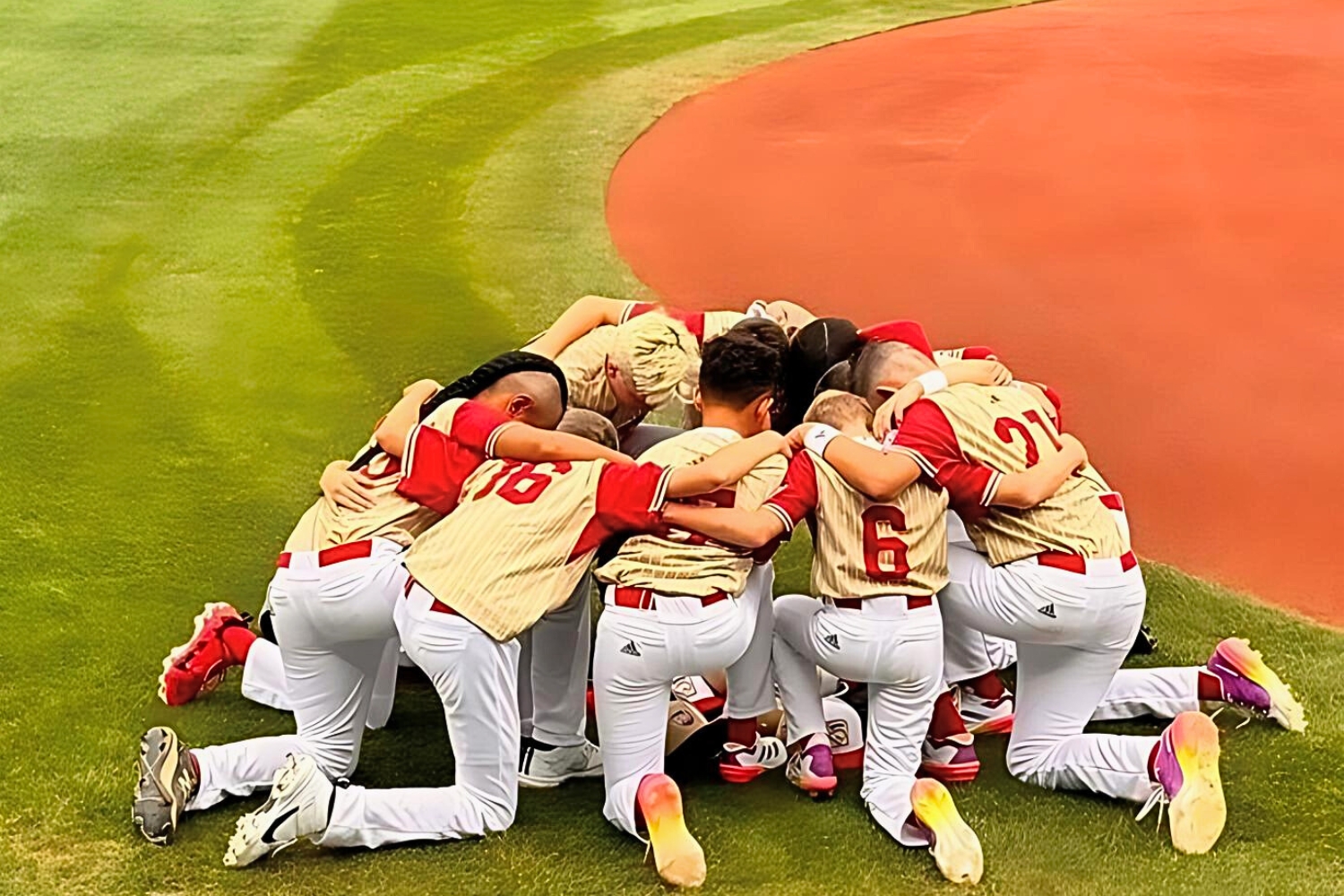 Henderson Little League kneel on baseball field. 