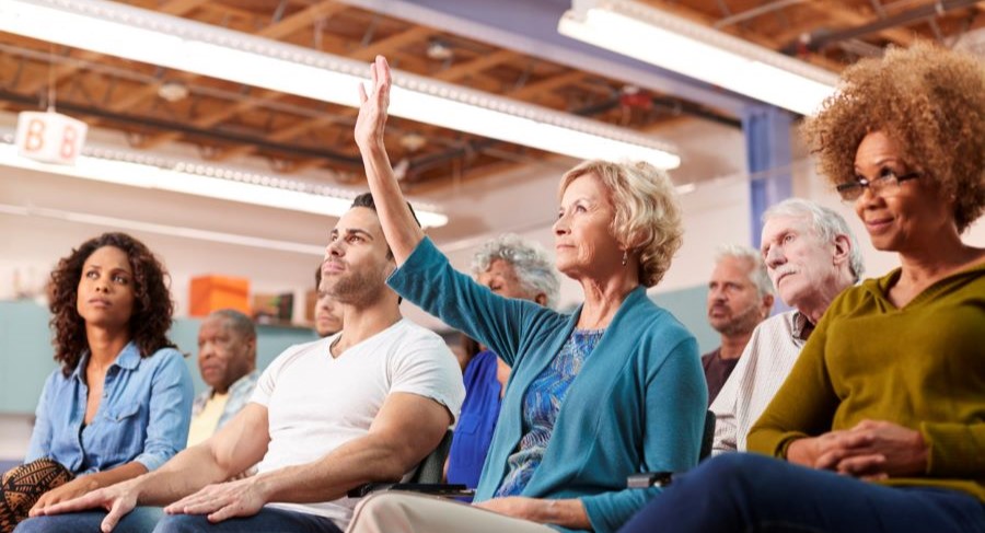 A group of people listening to a talk. A woman in the front raising her hand.