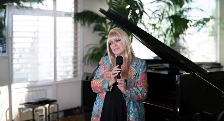 Rose Kingsley singing indoors by a piano.