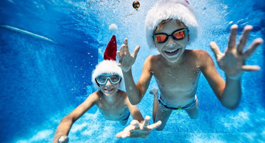 Two young boys swimming in Santa hats.